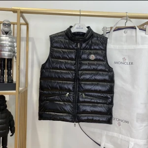 Svart dunväst från Moncler - Snygg Moncler väst lätt i tjockleken perfekt för sommaren med dragkedja och två fickor framtill och ger en stilren look. Moncler-logga på bröstet storlekar: XS-XL