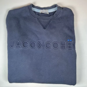 Mörkblå sweatshirt från Jacob Cohën Passar S,M - Snygg mörkblå sweatshirt från Jacob Cohën med broderad logotyp på framsidan. Tröjan har långa ärmar och ribbade muddar vid ärmslut och nederkant. Perfekt för en avslappnad stil.