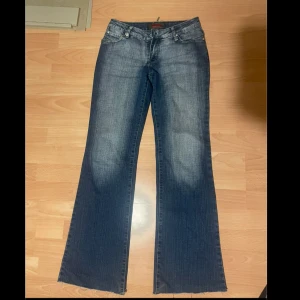 Vintage jeans - Snygga blå bootcut jeans med klassisk femficksdesign och slitna detaljer. Jeansen har en dragkedja och knapp framtill samt dekorativa sömmar på bakfickorna. Perfekta för en avslappnad stil. Passar mig som oftast bär strl 34 och är ca 160 cm. Low waist
