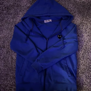 Blå hoodie från Comme des Garçons - Säljer en snygg blå hoodie från Comme des Garçons. Hoodien har dragkedja och en bekväm passform. Perfekt för en stilren och avslappnad look. Den är storlek XXs men passar även Xl i barn storlek. OBS TRÖJAN ÄR RESERVERAD 