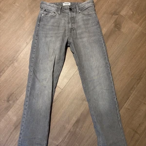 Grå jeans från Jack & Jones - Snygga grå jeans från Jack & Jones med klassisk femficksdesign. De har en rak passform och är tillverkade i ett bekvämt denimtyg. Perfekta för en avslappnad stil.