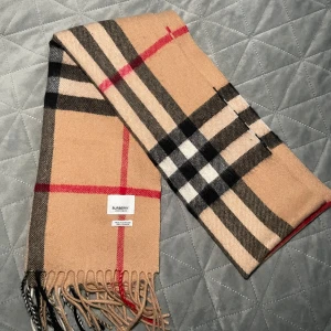 Burrberry halsduk!(100% Cashmere) - Snygg beige halsduk från Burberry med klassiskt rutmönster i svart, röd och vit. Tillverkad i mjuk kashmir och har fransar i ändarna. Perfekt för att hålla dig varm och stilren under kyliga dagar. Priset går möjligtvis att diskuteras! Inköpt i bulk av leverantör.                                               ⚠️OBS! Bundle pris finns nu tillgängligt för båda två halsdukarna. pris ligger på 1400kr!⚠️.                                                    Skriv gärna vid minsta fundering/R.EsellingSWE😎