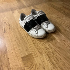Valentino Open sneakers i vitt och svart - Snygga Valentino Open sneakers i vitt med svarta detaljer. Skorna har en stilren design med snörning och en bred svart rem över ovansidan. Perfekta för en trendig look. Har använt skorna en del gånger och är i ett skick på kanske 6/10 och men dom funkar fortfarande perfekt och hur snygga som helst. Kartong följer med och säljer endast för 1199kr 