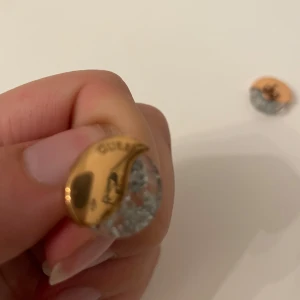 Guld och silver örhängen - Snygga örhängen i guld och silver med en glittrig design. De har en rund form och en elegant kombination av färger som ger en lyxig känsla. Perfekta för att lägga till lite extra bling till din outfit. Från GUESS 