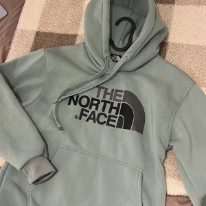 Grön hoodie från The North Face, storlek M - Snygg och trendig huvtröja från The North Face i en härlig grön färg. Tröjan har en klassisk design med en stor logotyp framtill. Perfekt för både vardag och fritid. Mycket bra skick på tröjan då den knappt är använd.