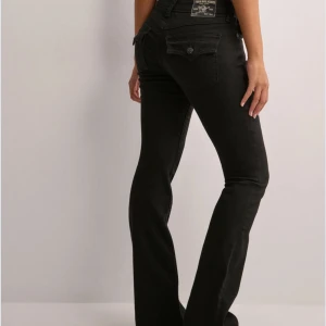 Svarta jeans från True Religion/nelly - Snygga svarta jeans från True Religion med bootcut-stil. De har en låg midja och klassiska femficksdetaljer med knappar på bakfickorna. Perfekta för en stilren look. De är lowwaisted. använda 2 gånger!!