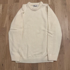 Stickad tröja från Zara - Säljer en stilren crèmefärgad stickad tröja från Zara. Tröjan har en klassisk rund halsringning och långa ärmar med ribbade muddar. Perfekt för kyligare dagar och lätt att matcha med olika outfits.
