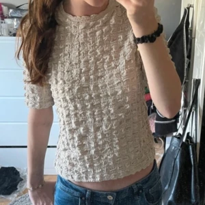 Beige ribbad topp - Säljer en beige ribbad topp med trekvartsärm. Toppen har en unik textur och är perfekt för både vardag och speciella tillfällen. Passar bra till jeans eller kjol.