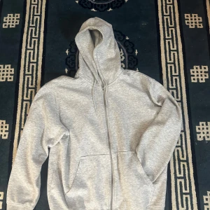 Grå hoodie från Weekday - Säljer en stilren grå hoodie från Weekday i storlek M. Den har en dragkedja framtill och en klassisk huva. Perfekt för en avslappnad look. Hör av er vid frågor!