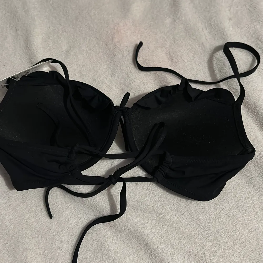 Snygg svart bikiniöverdel från cubus med knytband framtill och justerbara axelband. Perfekt för en dag på stranden eller vid poolen. Enkel och stilren design som passar till det mesta. Aldrig använd med prislapp kvar. Muu.