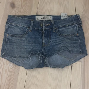 Blå jeansshorts från Hollister - Snygga blå jeansshorts från Hollister med fransiga kanter och klassisk femficksdesign. Perfekta för en avslappnad sommarlook. De har en lågmidjad passform och är tillverkade i slitstarkt denim.