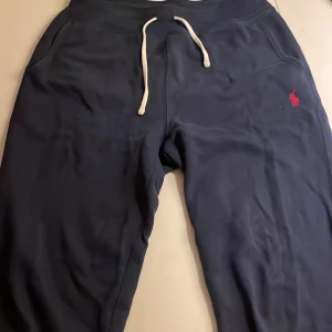 Mörkblå mjukisbyxor från Polo Ralph Lauren - Snygga mörkblå mjukisbyxor från Polo Ralph Lauren med en broderad röd logga. Byxorna har en bekväm passform med snörning i midjan och en bakficka. Perfekta för en avslappnad stil. Näst intill helt oanvända. Pris kan diskuteras vid en snabb affär.