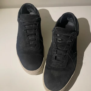 Svarta mocka skor från arigato - Snygga svarta sneakers från Axel Arigato i mocka med vit sula. Skorna har en stilren design med snörning och diskret branding på sidan och sulan. Perfekta för en minimalistisk look.