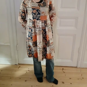 Mönstrad klänning i bohemisk stil - Säljer en unik bohemisk klänning med ett färgglatt mönster i orange, blått och beige. Klänningen har en lös passform och långa ärmar, perfekt för en avslappnad stil. Den är tillverkad i ett mjukt material som ger en bekväm känsla hela dagen.