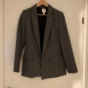 Grå kavaj från H&M - Snygg grå kavaj från H&M i klassisk design. Perfekt för en stilren look med sina långa ärmar och diskreta fickor. Passar utmärkt till både vardag och mer formella tillfällen. Pris går att diskutera vid snabb affär. Kontakta gärna mig om du har frågor eller funderingar 