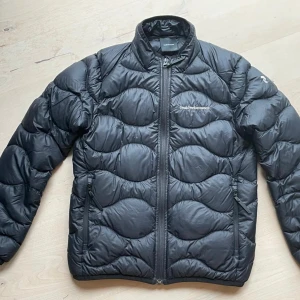 Svart dunjacka från Peak Performance - Säljer en svart dunjacka från Peak Performance med dragkedja framtill och två sidofickor. Jackan har en quiltad design och långa ärmar, perfekt vårjacka.