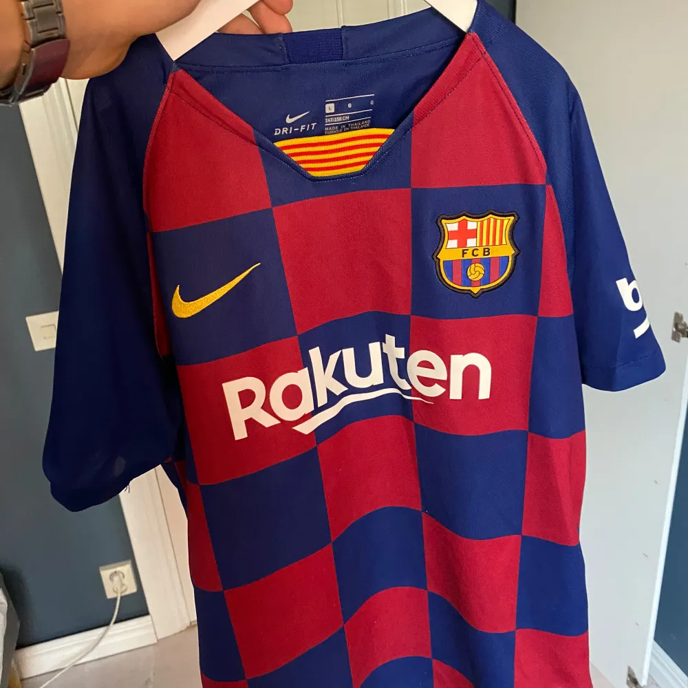 Säljer en snygg FC Barcelona fotbollströja från Nike i blårött rutmönster. Tröjan är kortärmad och har klubbens emblem på bröstet samt sponsorer som Rakuten och Unicef. Perfekt för alla Barca-fans! Årsmodellen är 2019/2020 den är självklart äkta!. T-shirts.