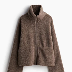 Brun teddyjacka - Mysig brun teddyjacka med dragkedja och hög krage. Perfekt för kyliga höst- och vinterdagar. Jackan har en avslappnad passform och stora fickor framtill. Superbekväm och stilren!