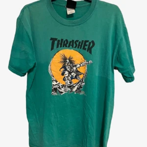 Grön Thrasher t-shirt - Säljer en grön Thrasher t-shirt med ett coolt tryck av en skateboardåkare framför en stor orange sol. Perfekt för skateparken eller som en avslappnad vardagslook. T-shirten är kortärmad och gjord i mjuk bomull. Passar perfekt till jeans eller shorts!