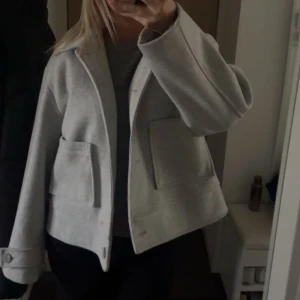 Ljusgrå kappa - Säljer en stilren ljusgrå kappa i normal passform. Den har långa ärmar och knappar framtill. Perfekt för höst och vår, med en klassisk look som funkar till det mesta. Den är i storlek xl men sitter mer som en m/l💕