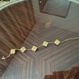 Guldarmband med blommotiv guldplaterad - Säljer ett elegant guldarmband med fem blommiga detaljer. Perfekt för att ge en touch av glamour till vilken outfit som helst. Armbandet har en fin kedja och är lätt att justera i storlek. Passar både till vardag och fest!