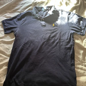 mörkblå pikétröja från Ralph Lauren - Säljer en klassisk svart pikétröja från Ralph Lauren. Den har korta ärmar och en liten broderad logga på bröstet. Perfekt för både vardag och fest. Skön och stilren design som passar till det mesta. Hör av dig vid intresse!