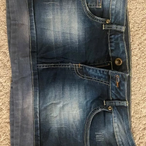 Blå jeanskjol - Säljer en cool blå jeanskjol med slitna detaljer och klassiska femficksdesign. Kjolen har en knapp och dragkedja framtill och är perfekt för en avslappnad vardagslook. Passar bra till både sneakers och sandaler. Perfekt för sommardagar! 💙