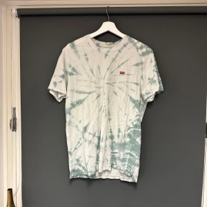 Tie-dye t-shirt från Levi's - Säljer en supercool tie-dye t-shirt från Levi's i grönt och vitt. Den har en normal passform och är kortärmad, perfekt för sommaren. Levi's-loggan är snyggt placerad på bröstet. Perfekt för en avslappnad stil!