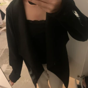 Svart kappa - Säljer en stilren svart kappa i normal passform. Perfekt för både vardag och fest. Den har långa ärmar och en enkel design som gör den lätt att matcha med olika outfits. Ett måste i garderoben för en klassisk look! Har knutit där bak då det är därför den sitter så fint!