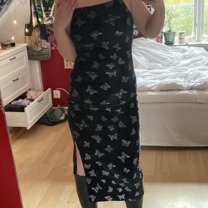 Midi klänning med fjärilar - En lång svart klänning i sammet med glittriga, silvriga fjärilsdetaljer! Knappt använd och sitter tight, inget blixtlås. Har även en slit på ena sidan! 