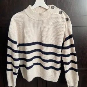 Stickad tröja med knappar på axeln från Bondelid. Off-white med mörkblå ränder. Mycket bra skick. Normal i storlek.   Modell: Angelicka stripe knit