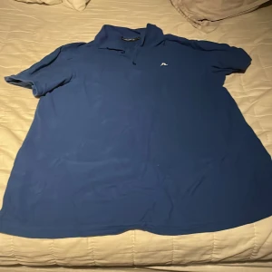 Blå pikétröja från J.Lindeberg - Säljer en snygg blå pikétröja från J.Lindeberg i storlek M. Perfekt för både vardag och lite finare tillfällen. Tröjan har korta ärmar och en klassisk krage med knappar. Den är i bra skick och redo för nya äventyr! Köpt vid center syd