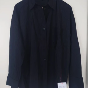 Svart skjorta med vita ränder (oanvänd) - Helt oanvänd svart skjorta från Topshop med tunna vita ränder och ficka på bröstet. Prislappar kvar. Originalpris 709 sek. 