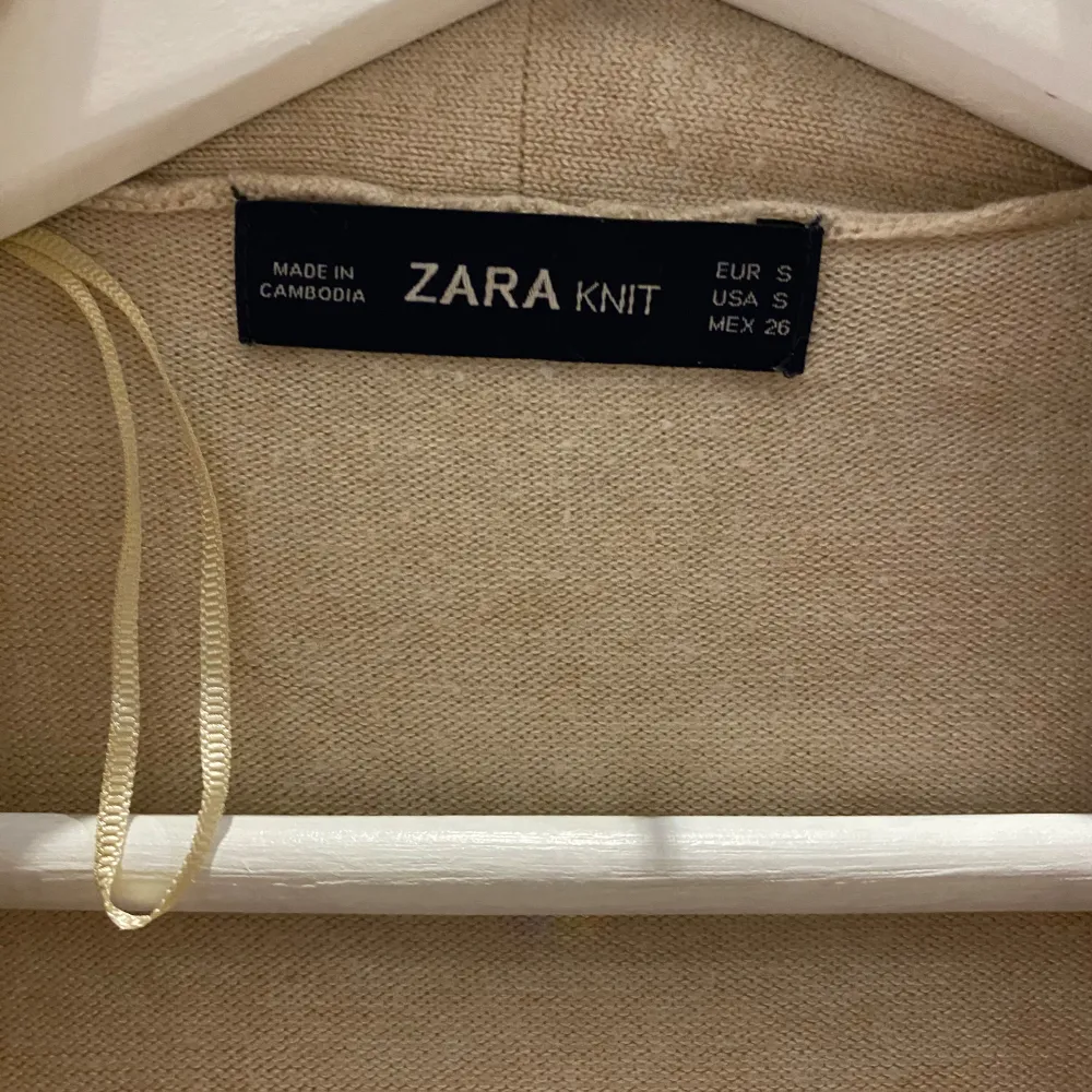 Säljer en superfin beige stickad kofta från Zara. Den har långa ärmar och ett knytband i midjan för en snygg passform. Perfekt för höst och vår när det är lite kyligt ute. Koftan är i nyskick och väldigt bekväm att ha på sig. Passar både till vardags och lite mer uppklädda tillfällen.. Stickat.