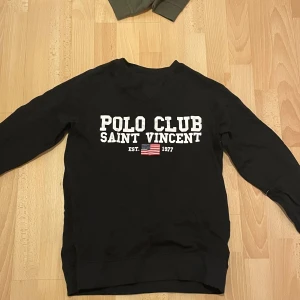 Svart tröja från Polo Club Saint Vincent - Säljer en svart tröja från Polo Club Saint Vincent med vit text och en liten amerikansk flagga på framsidan. Tröjan är oanvänd och helt ny