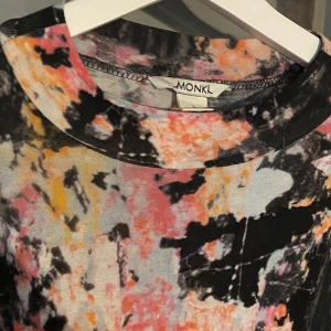 Färgglad klänning från Monki - Säljer en supercool klänning från Monki med ett abstrakt mönster i svart, rosa, orange och gult. Klänningen har trekvartsärmar och en avslappnad passform. Perfekt för en färgglad dag eller en festlig kväll!