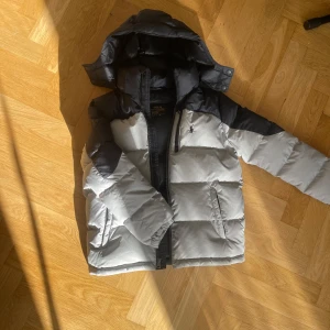 Grå och svart pufferjacka från Polo Ralph Lauren - Säljer en snygg och varm puffjacka från Polo Ralph Lauren. Superbra skick, som ny. Storlek M (150), Köpt på Plick men insåg att den var för liten.