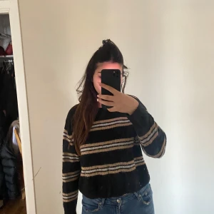 Svart och beige randig tröja - Säljer en snygg svart tröja med beige och vita ränder. Den är perfekt för höst och vinter med sin mysiga och varma känsla. Tröjan har långa ärmar och en normal passform. Perfekt för en avslappnad stil!