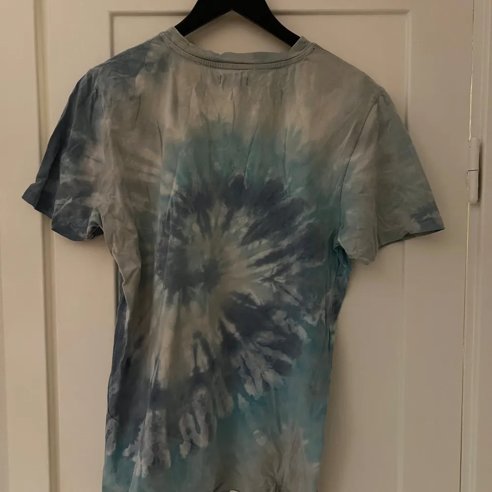 Säljer en supercool tie-dye t-shirt. Den har en blå och vit spiraldesign som ger en riktigt chill vibe. Perfekt för sommardagar eller festivaler. T-shirten är kortärmad och har en bröstficka för extra stilpoäng. Skön och avslappnad passform!. T-shirts.