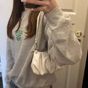 Vit axelväska i syntetmaterial - Säljer en superfin vit axelväska i syntetmaterial. Den har en snygg rynkad design och en praktisk dragkedja upptill. Lite finare väska med utrymme för det nödvändiga plus lite till, perfekt till en utekväll 