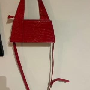Röd handväska - Röd handväska från gina tricot! Jättefin väska med snygga detaljer! Krokodilmönstrad väska med handtag upptill. Väskan är röd och har silverdetaljer. Den har lång, avtagbar axelrem och dragkedjestängning upptill. Slutsåld på hemsidan!!! Nypris 359 