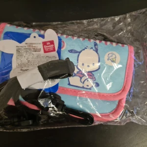 Blå och rosa Pochacco axelväska - Säljer en supergullig axelväska med Pochacco-motiv från Sanrio. Väskan är i en härlig blå färg med rosa accent och har ett sött tryck av Pochacco. Perfekt för att bära med sig småsaker på resan eller stranden.