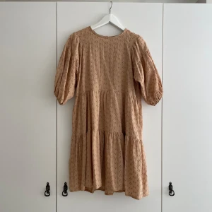 Klänning i spets  - Rosa/beige klänning i en slags spets med mönster av blommor. Supergullig! Bandet som man drar över knappen gick tyvärr av, men nog lätt att sy fast igen.  Är i storlek M, men passar S med. 