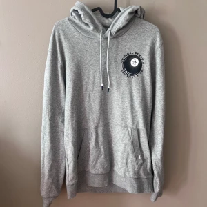 Grå hoodie från Original Penguin - Säljer en snygg och bekväm grå hoodie från Original Penguin. Den har en klassisk design med en känguruficka och justerbar dragsko i huvan. Perfekt för en avslappnad stil och passar till alla tillfällen. Tillverkad i Bangladesh.