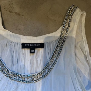 Linne - Ilse Jacobsen - Ett festligt linne från Ilse Jacobsen med diamanter längs hela urringningen och passar både på fest och en mysigare sommarkväll. 