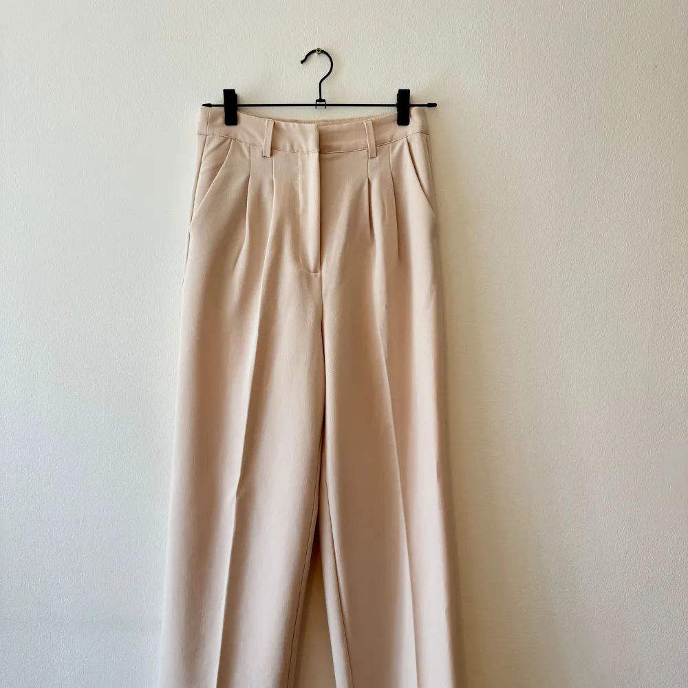 Säljer ett par stilrena beige kostymbyxor från BikBok i storlek 36. Byxorna har en hög midja och en rak passform som ger en elegant look. Perfekta för både kontoret och festligare tillfällen. De är i nyskick och redo att bäras med stil!. Jeans & Byxor.