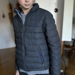 Dunjacka Ralph Lauren st 146-152, 10-12 år  - Mycket fin grå dunjacka Ralph Lauren, st M, ca 146-152, passar ca 10-12 år.  Mycket sparsamt använd då sonen hade en likadan jacka i annan färg.  Hämtas även vid Östermalmstorg alt Gärdet.  Mvh Cecilia 