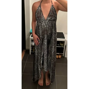 Mönstrad långklänning med öppen rygg - Oregelbunden silke långklänning med ett unikt mönster i silver, vit och mörkrosa. Klänningen har en djup v-ringning och knytband runt nacken, vilket ger en snygg halterneck-stil och även  öppen rygg. 