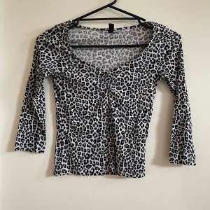 Leopardmönstrad topp med trekvartsärm - Snygg leopardmönstrad topp med trekvartsärm. Perfekt för en cool och trendig look. Toppen har en v-ringad design och är i ett stretchigt material för en bekväm passform.