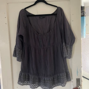 Grå blus från Lindex - Säljer en snygg grå blus från Lindex i storlek 42. Den har trekvartsärmar och fina spetsdetaljer vid ärmslut och nederkant. Perfekt för både vardag och fest!